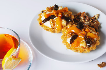 Basket-cake with nuts, dried fruits and jelly on white plate. Cup of tea. Closeup. Selective focus.