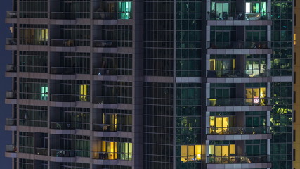 Fototapeta na wymiar Glowing windows in multistory modern glass and metal residential building light up at night timelapse.