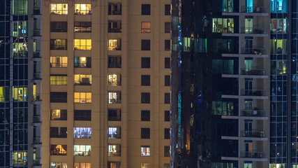 Glowing windows in multistory modern glass and metal residential building light up at night timelapse.
