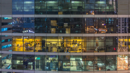 Glowing windows in multistory modern glass and metal office building light up at night timelapse.