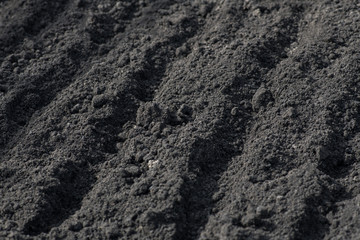 Empty furrows on black ground in a farm field in early spring. Preparation of soil for planting seeds. Horizontal photography.