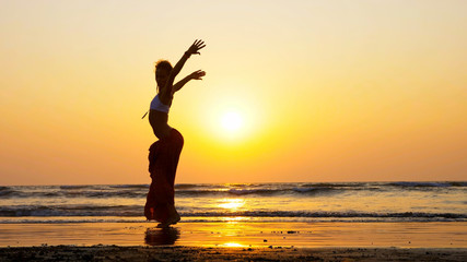 Fototapeta premium Silhouette of young girl dancing on the beach at sunset