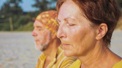 Fototapeta premium Close-up portrait of senior couple sits and meditating together on sandy beach