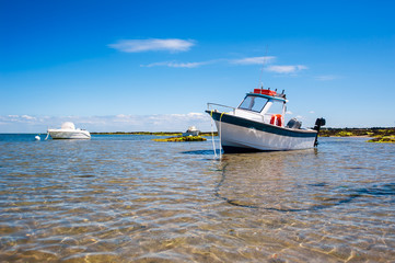 White boat on sand surrounded with water and rocks in summertime in Noirmoutier