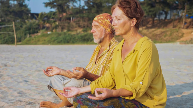 Senior couple sits and meditating together on sandy beach