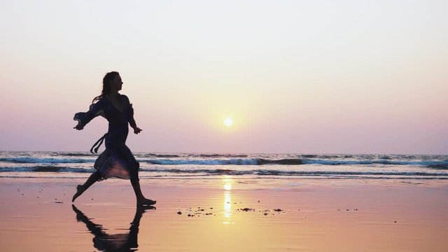Silhouette of young woman performing grand jete jump on the beach in slow motion