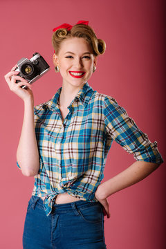Portrait of a girl dressed in vintage clothing holding old fashioned camera on the pink background. Pinup portrait
