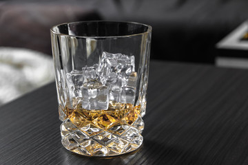 Glass of whiskey with ice cubes on black table