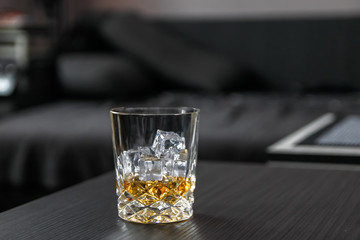 Glass of whiskey with ice cubes on black table