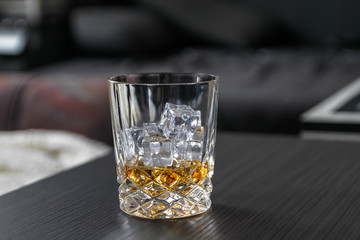 Glass of whiskey with ice cubes on black table