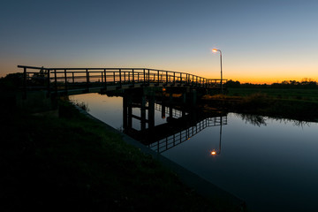 Bicycle bridge with lantern over a canal in The Netherlands after sunset.