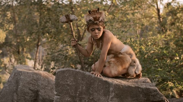 Caveman, manly boy with primitive weapon outdoors. Ancient prehistoric warrior.