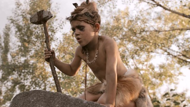 Caveman, manly boy with primitive weapon outdoors. Ancient prehistoric warrior.