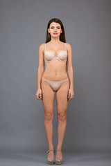 Fototapeta premium Full length portrait of beautiful brunette women with a slim figure in light underclothing. Model snaps in the studio on gray background