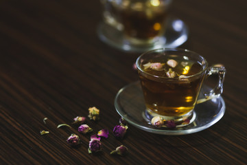Rose oriental tea in transparent glass cups on dark wood background.