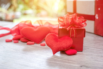 Gift box with red bow ribbon and paper heart on wooden table for Valentines day.