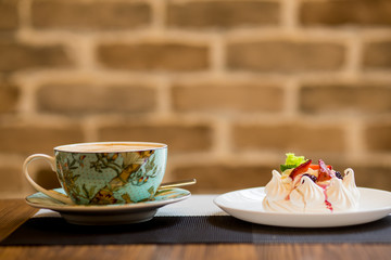 Cup cappucino with heart coffee art a light and airy pavlova's dessert with merengue and fruit