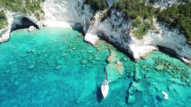  Aerial drone bird's eye view video of iconic tropical rocky paradise bay called blue lagoon with caves and turquoise clear waters visited by sail boats, island of Paxos, Ionian, Greece