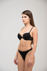 Obraz premium Three-quarter portrait of beautiful brunette women with a slim figure in black bra and thong. Model snaps in the studio on white background
