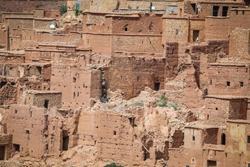 Old Berber village with mud brick architecture in the green oasis of a river valley surrounded by the arid desert landscape of the Atlas Mountains in Morocco.