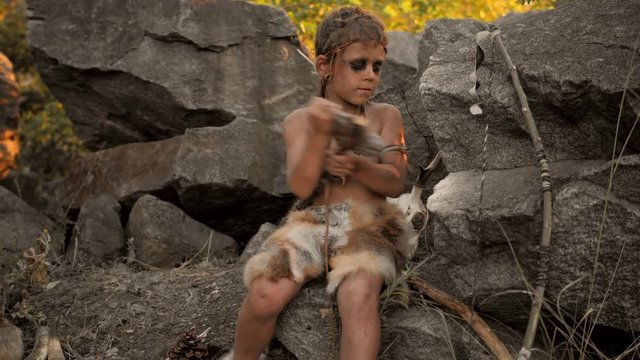 Caveman, manly boy making primitive stone weapon in camp
