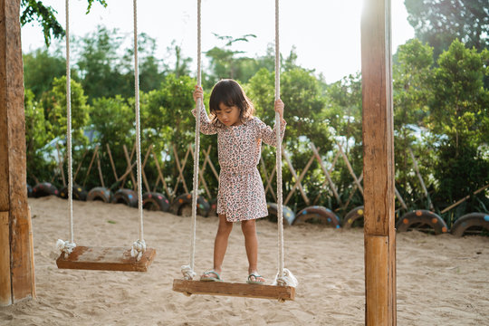 a little girl standing on the wooden swing alone 