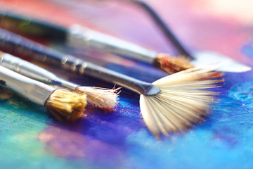 Fototapeta premium Several brushes with different bristles and palette knife lie on the palette, painted with blue, pink and purple oil
