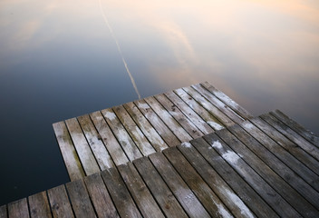 Old rustic pier bridge on a black lake with a sky reflection. Ripples in water.