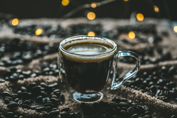 cup of coffee and coffee beans on textile surface with lights on background