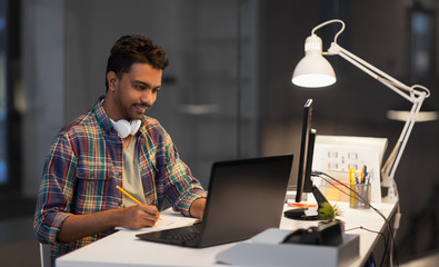 deadline, technology and people concept - creative man with laptop computer working at night office...