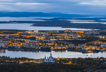 Panoramic view of northern city Monchegorsk with beautiful evening illumination located among mountains, taiga forest and many lakes. Orthodox cathedral on foreground. Kola peninsula, Russia