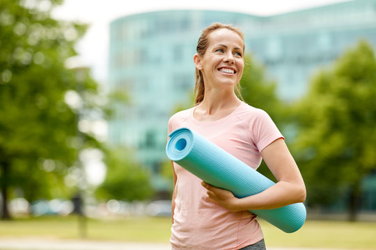 fitness, sport and healthy lifestyle concept - happy smiling woman with exercise mat at city park