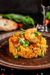 Concept of Spanish cuisine. Paella with seafood and shrimps, with green peas in a clay plate. A glass of cool wine is on the table. background image, copy space
