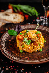 Concept of Spanish cuisine. Paella with seafood and shrimps, with green peas in a clay plate. A glass of cool wine is on the table. background image, copy space