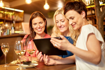 leisure, technology and lifestyle concept - happy women with tablet pc computer at wine bar or...