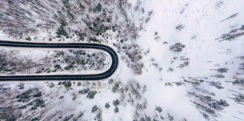 Curvy windy road in snow covered forest, top down aerial view. Winter landscape.
