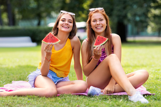 leisure and friendship concept - happy smiling teenage girls or friends eating watermelon at picnic in summer park