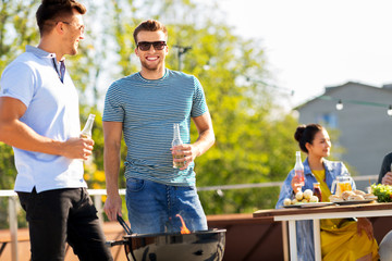 leisure and people concept - happy friends with bbq grill and non-alcoholic drinks having barbecue party on rooftop in summer