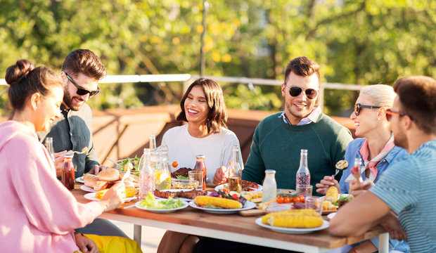 leisure and people concept - happy friends eating and drinking at rooftop party in summer