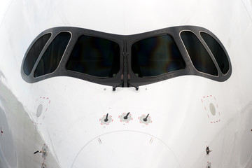 Close front outside view of a white big jet plane cockpit.