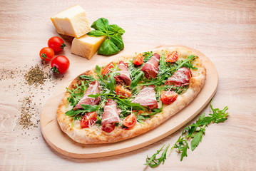 Pizza on Tabletop. Pizza wiht bacon, tomatoes, basil and arugula.