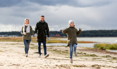 family, leisure and people concept - happy mother, father and little daughter walking along autumn beach