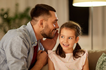 family, fatherhood, leisure and people concept - happy father whispering secret to daughter at home in evening