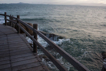 Sea waves foam on the stones below wooden plank bridge