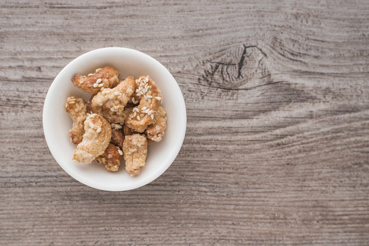 Sugar-coated cashews with white sesame seeds in a white bowl on a wooden background.