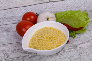 Raw couscous in the bowl served salad leaves, tomato and pepper
