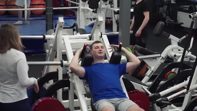 Female trains newbie first day in the gym trying Hack leg press squat. Face expression