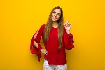 Young girl with red dress over yellow wall showing and lifting a finger in sign of the best