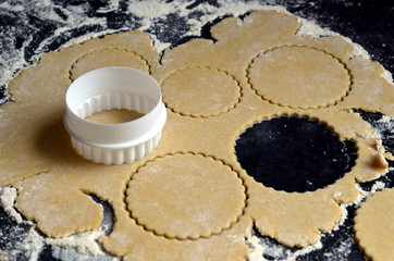 White cookie cutter on rolled out pastry on dark floured counter