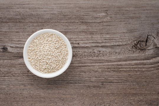 Sesame seeds in a small white bowl on a wooden background, culinary ingredients
